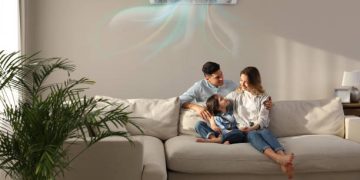 Happy family resting under air conditioner on beige wall at home